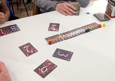 Players aiming for the second highest card in Schadenfreude, the strategic trick-taking game from Japan.